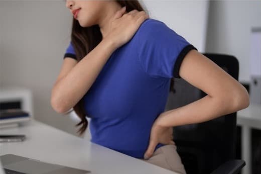 Person holding her neck and lower back at a desk